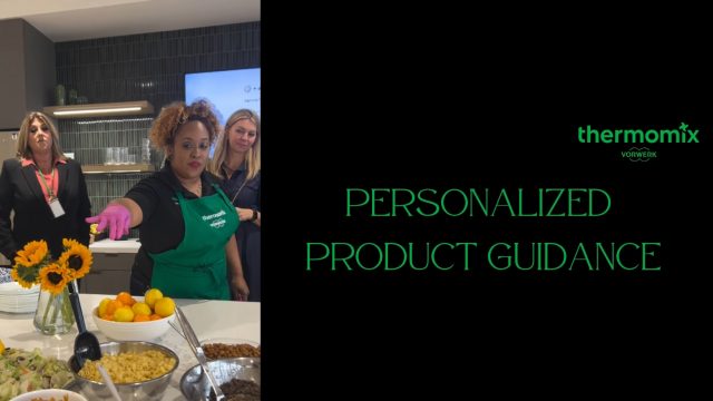 A-Thermomix-consultant-in-a-green-apron-offers-product-guidance-to-attendees-at-a-kitchen-demo-with-food-and-sunflowers-on-the-counter